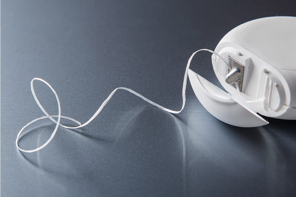 Nærbilde av tanntråd i hvit beholder på mørk overflate. Viktig tannhelseverktøy for rengjøring mellom tennene.