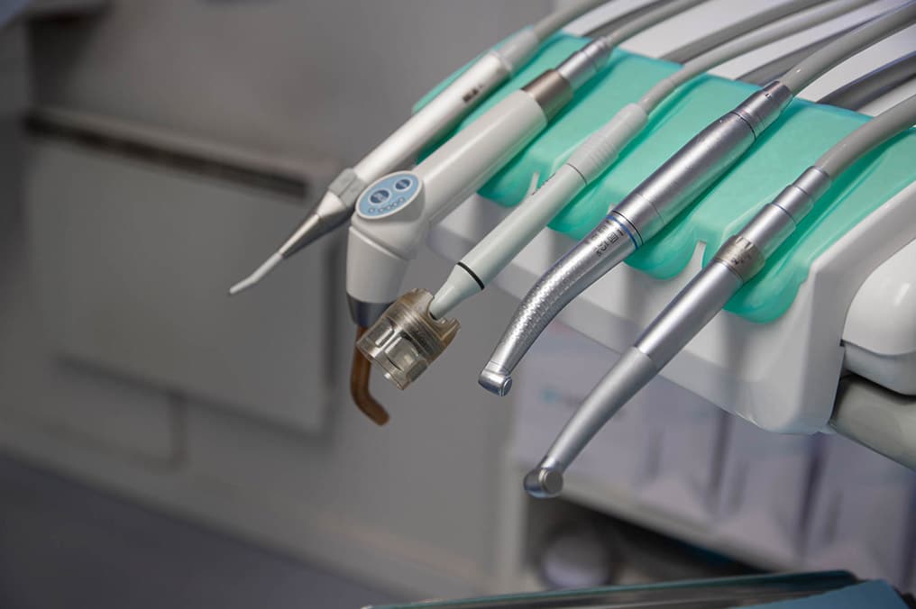 Nærbilde av ulike tannlegeinstrumenter som bor og renseverktøy anrettet på en hygienisk holder i et behandlingsrom.