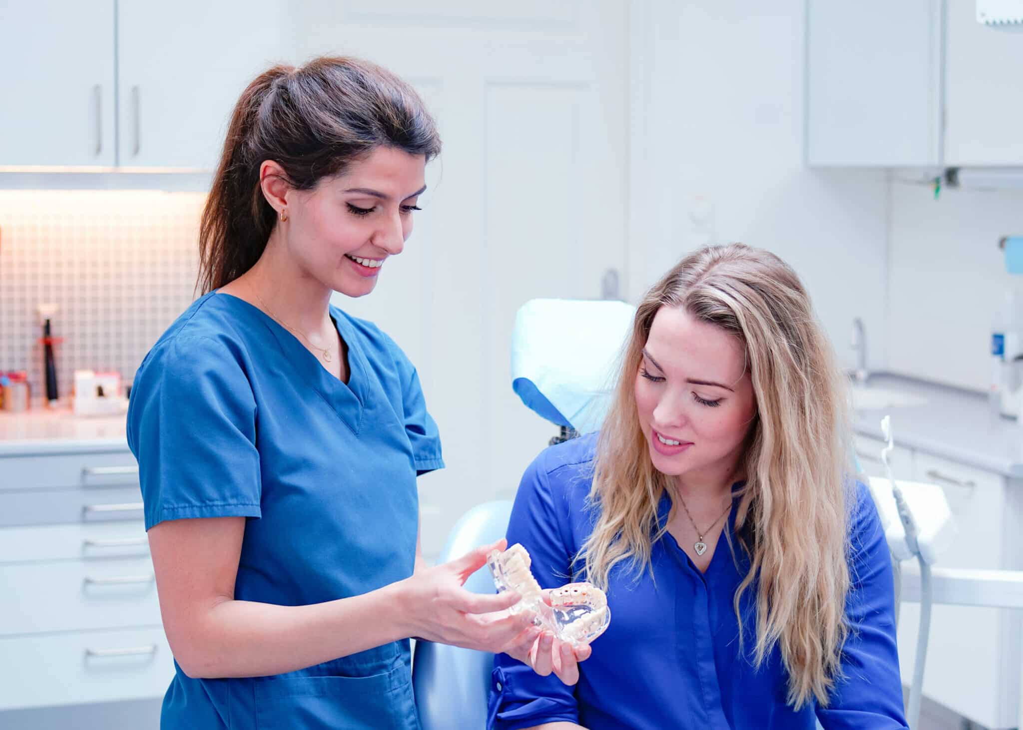 Tannlege viser pasient tannmodell og forklarer tannbehandling i detalj. Fokus på pasientinformasjon, implantat eller bittjustering.