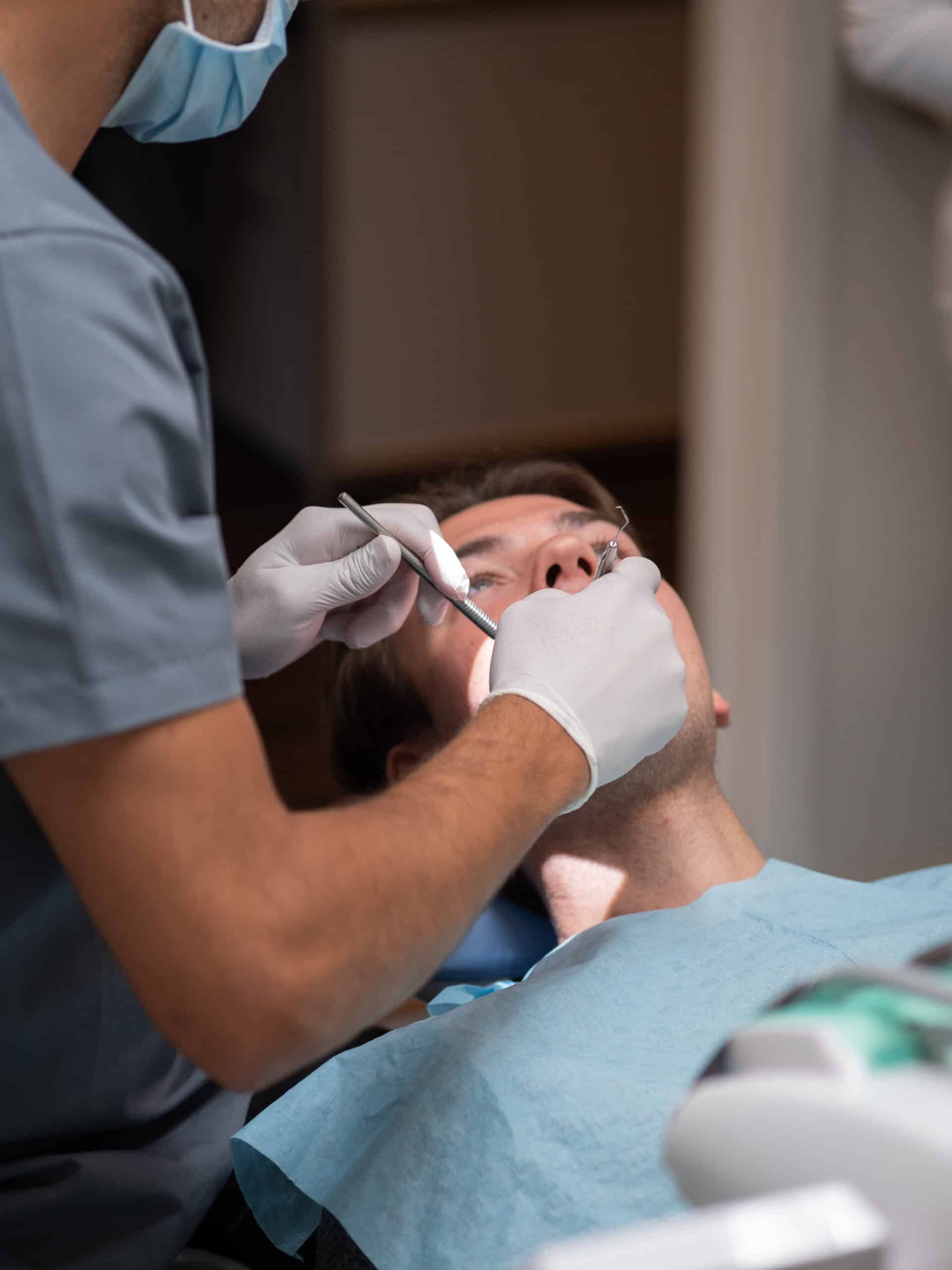 Nærbilde av tannlege i arbeid med pasient, som ligger i behandlingsstol med beskyttelsesduk. Fokus på presis tannbehandling og hygiene.